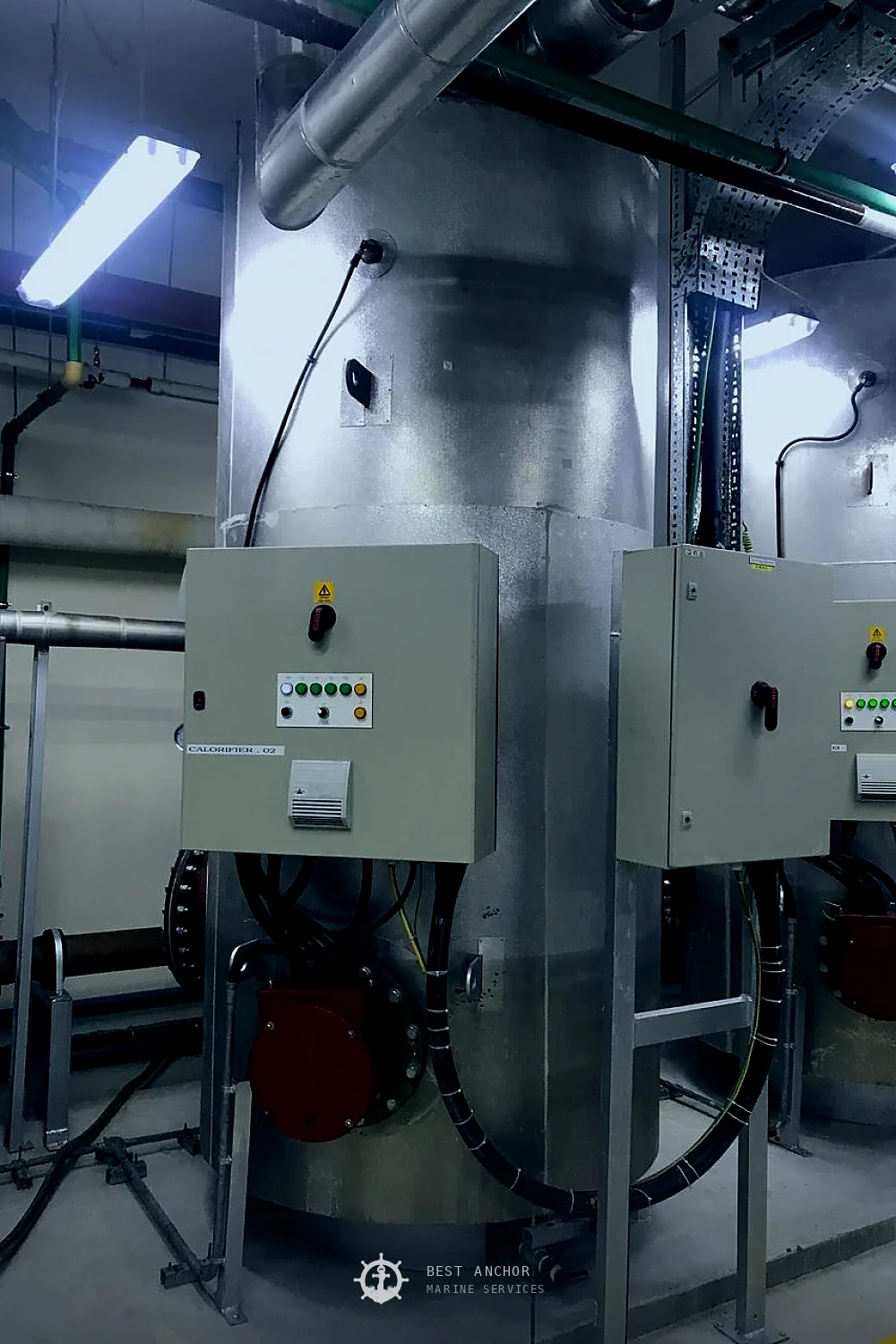Two insulated hot water calorifiers in a plant room, each fitted with a flanged immersion heater terminal head and its own local control panel